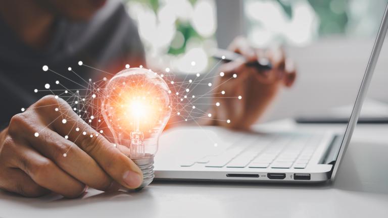 Person at a laptop with a lit light bulb in the right hand